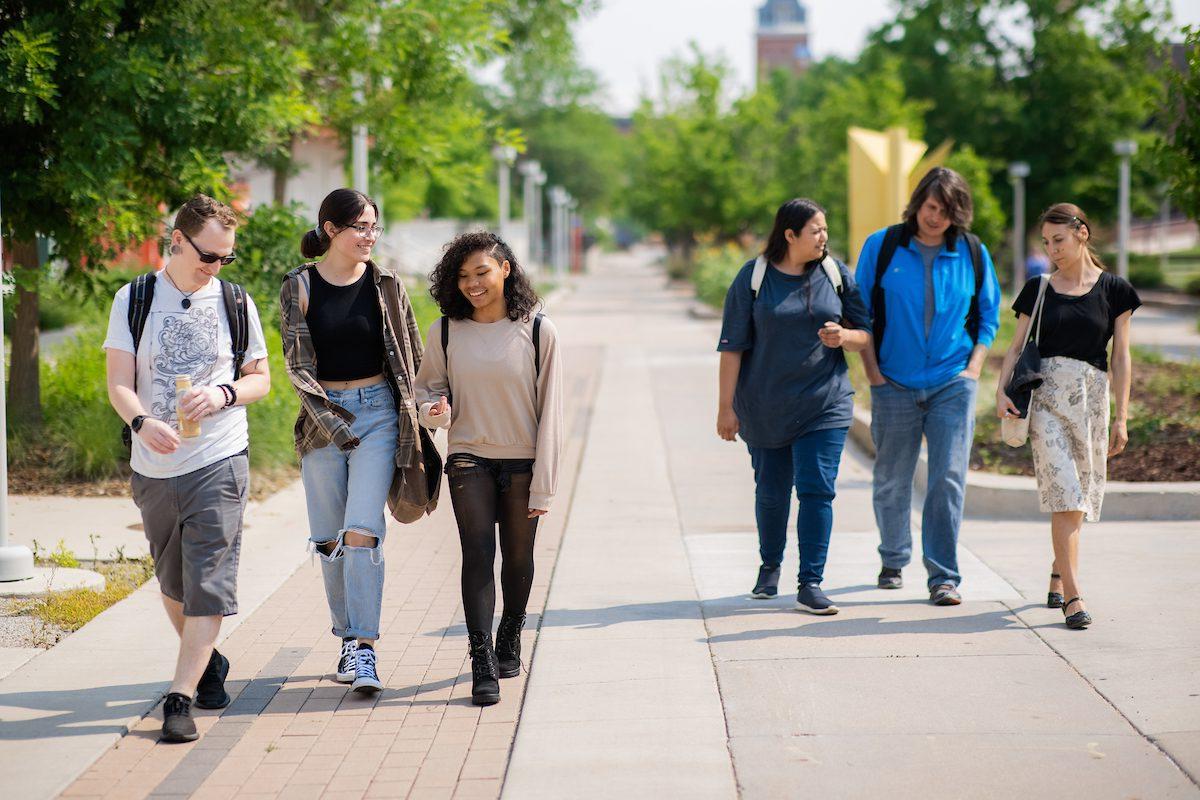 six students of walk together on a sidewalk near the library.